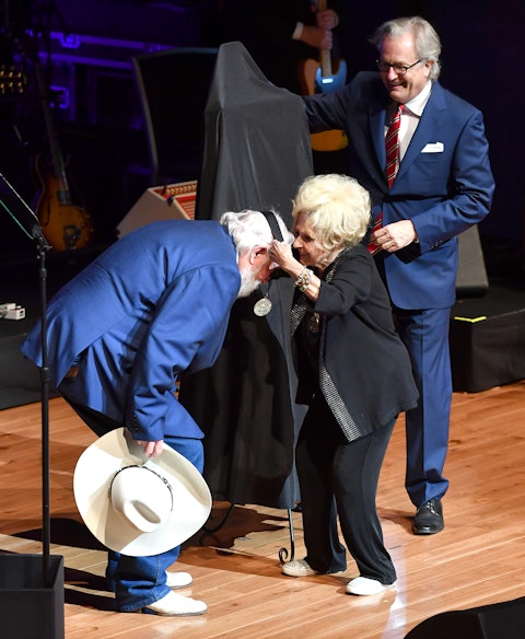 Charlie Daniels leans as Brenda Lee places a Medallion around his neck, signifying membership in the Country Music Hall of Fame. Looking on is Kyle Young, CEO of the Country Music Hall of Fame and Museum. The 2016 Medallion Ceremony, held October 16 in the museum’s CMA Theater, marked the official induction of Daniels, producer and record company owner Fred Foster, and singer Randy Travis. Photo by Jason Davis.