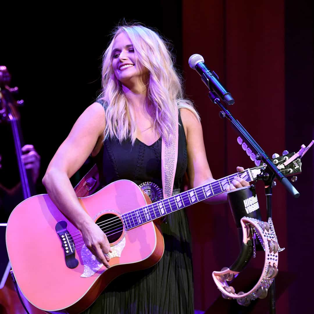 Miranda Lambert smiling on stage as she plays a guitar.