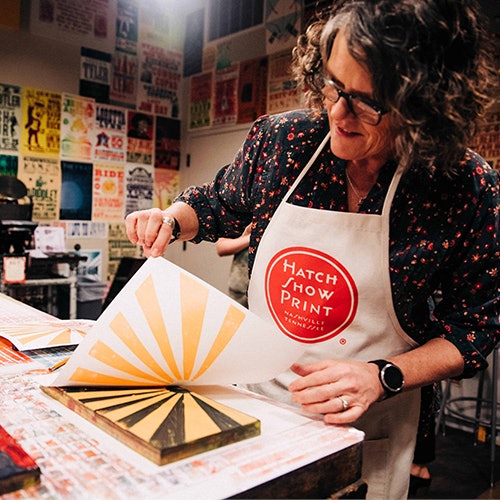 Hatch Show Print Block Party. Photo of a woman in a Hatch Show Print apron making a print design.