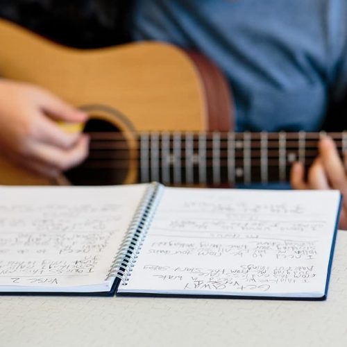 Family Program: Songwriting 101 Workshop. Photo of music in front of someone playing the acoustic guitar.