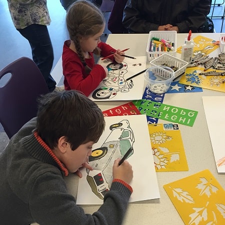 Photo of two children coloring and decorating cars and motorcycles on a paper medium.