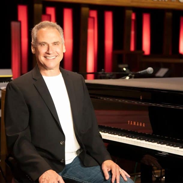 Photo of Randy Hart smiling at the camera in front of a piano