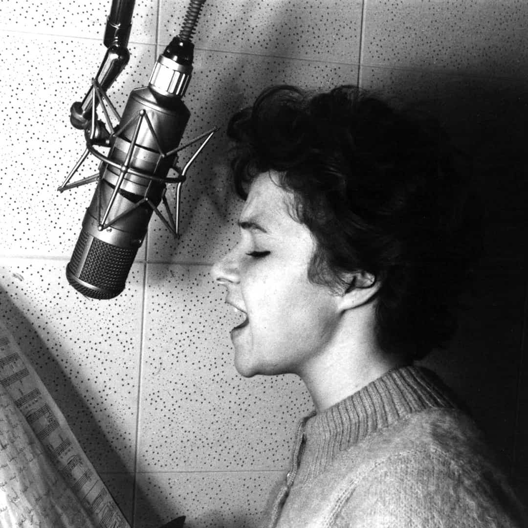 Brenda Lee recording on a microphone with sheet music in front of her