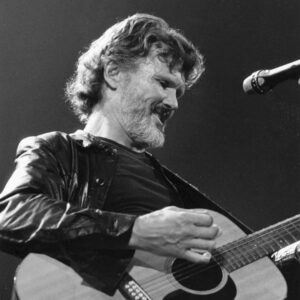 Kris Kristofferson playing on a classical guitar on stage.