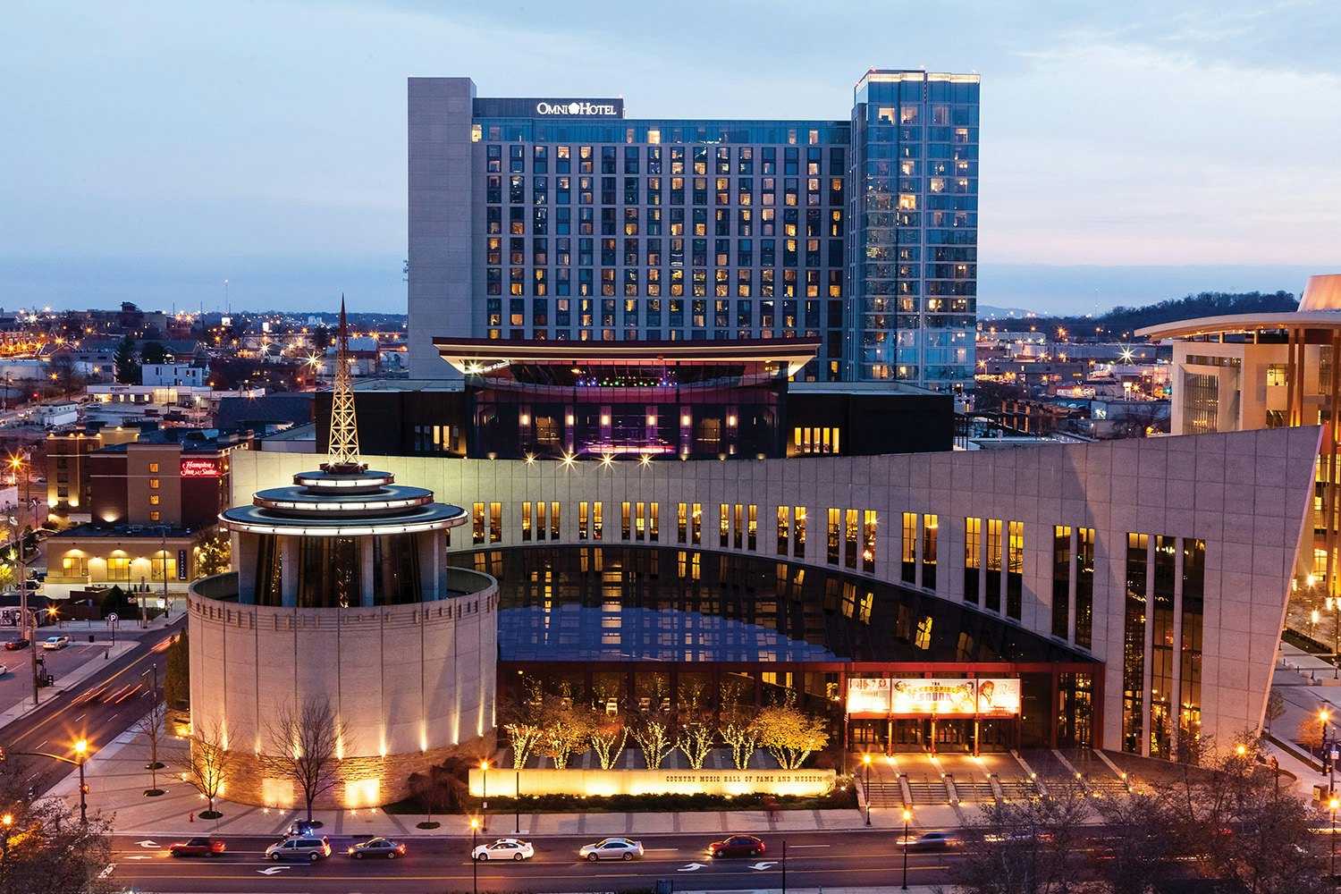 Exterior, night photo of the Country Music Hall of Fame and Museum with the Omni Hotel in the background.