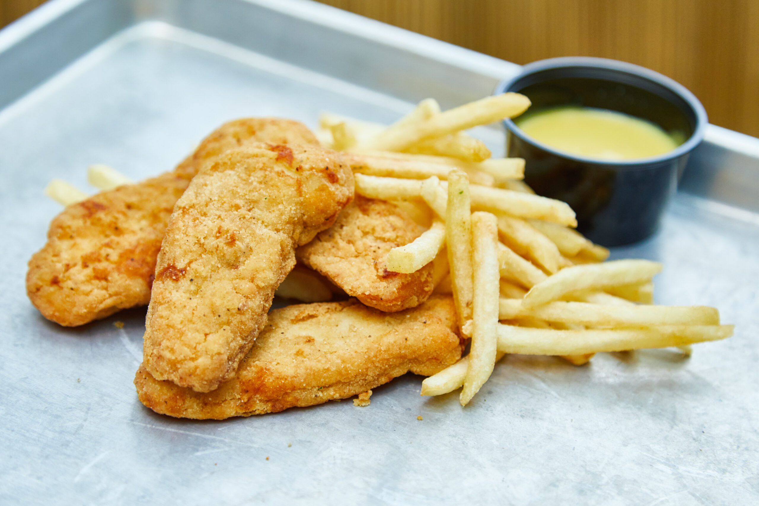 Chicken tenders with french fries and a side of honey mustard sauce served on a metal tray