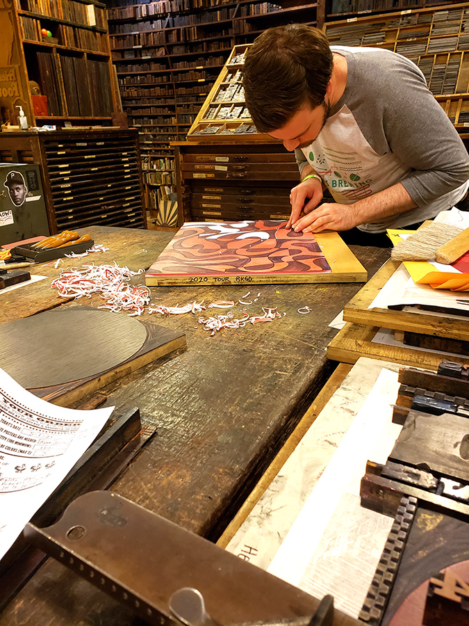 Man carving a design into a printing block that will be used to make a custom poster