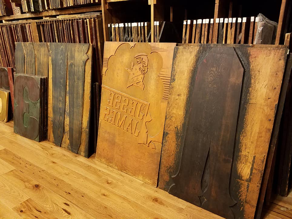 Four Very Large printing blocks sitting on the floor leaned against a wall of printing blocks.