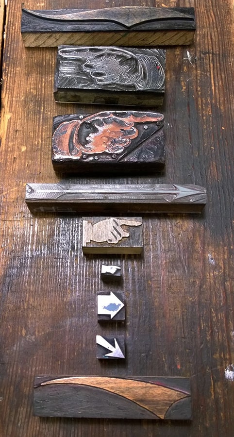 A collection of our historic printing blocks laid out in a line. Each of the blocks indicates direction via arrows or pointed fingers on a hand.