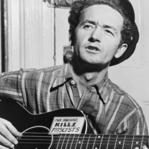 Woody Guthrie playing acoustic guitar was a sticker that reads "This Machine Kills Fascists"