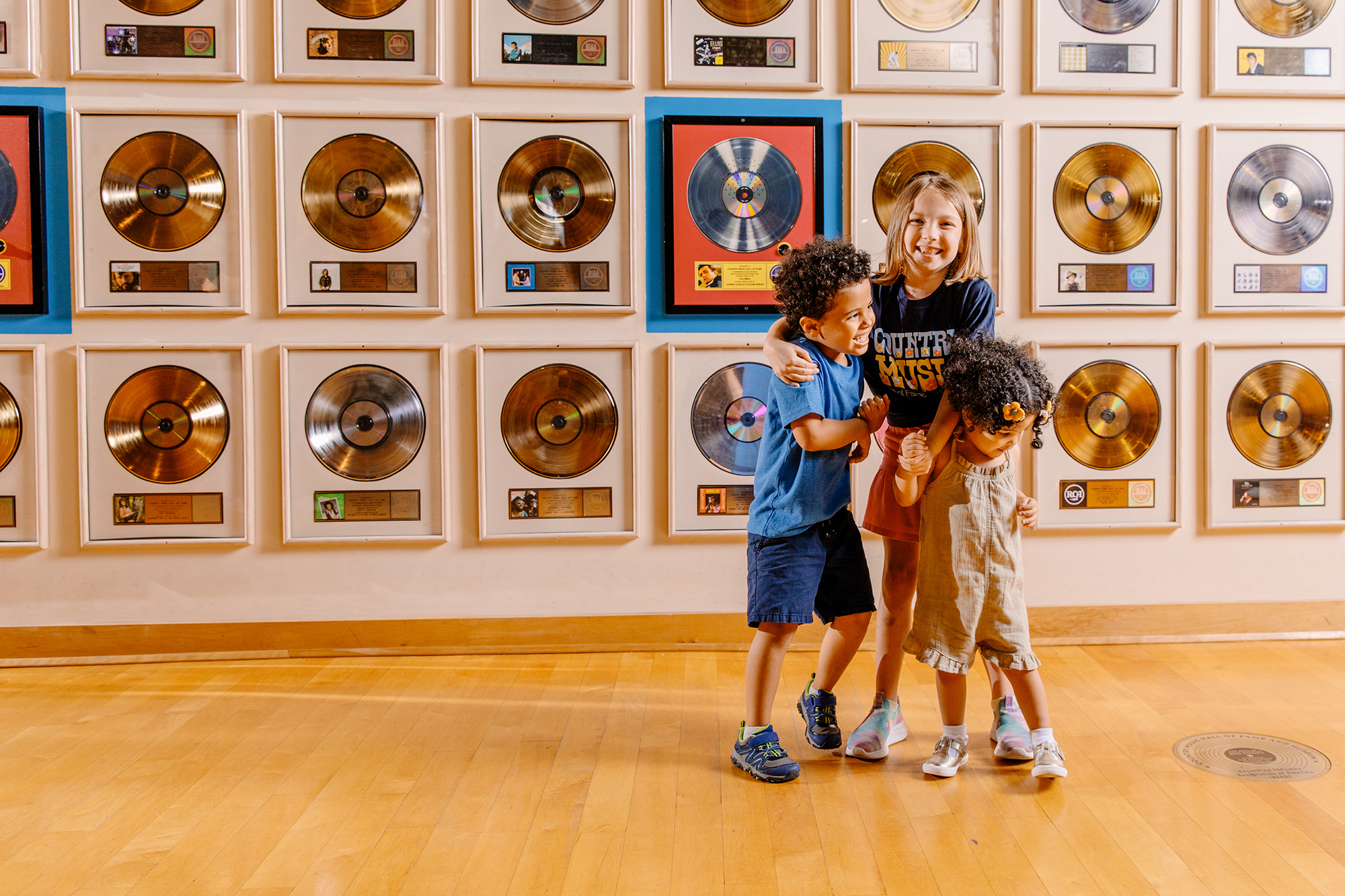 Three children laugh infront of a wall full of gold records.