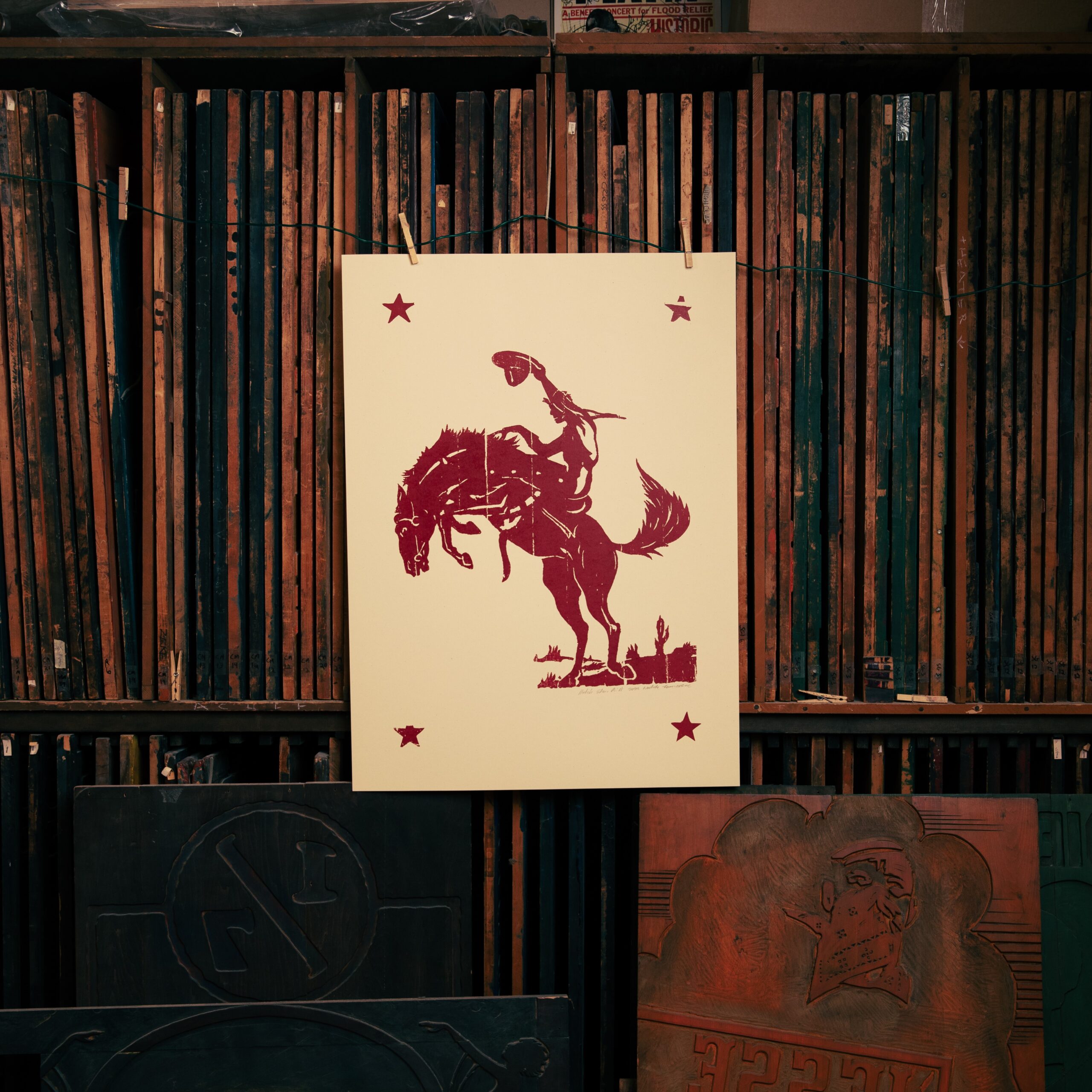 Print of a cowboy on a horse hangs on a wall of printing blocks.
